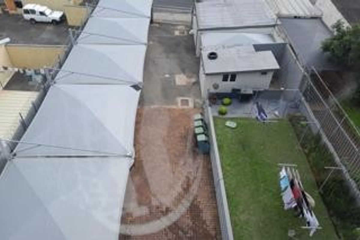 Aerial view of the property exterior featuring a paved driveway with shade sail carports, a small lawn area, and an outbuilding.