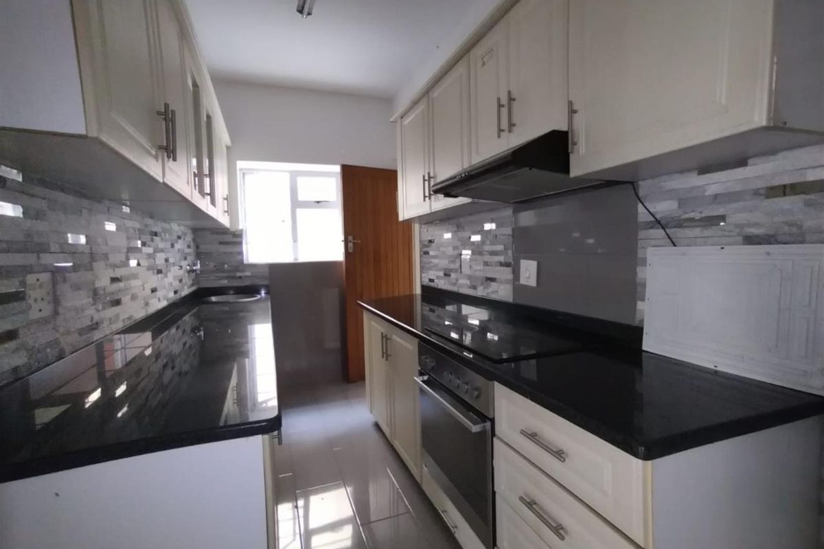 A clean, galley-style kitchen featuring granite countertops, built-in cabinetry, a modern oven, and a sleek tiled backsplash.