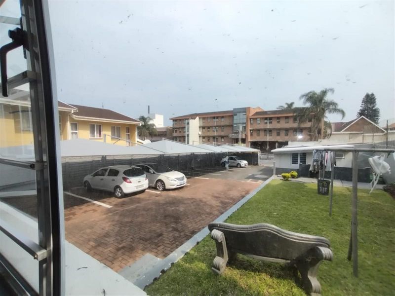 View of the rear exterior area featuring a paved driveway, covered parking bays, and a small lawn area.