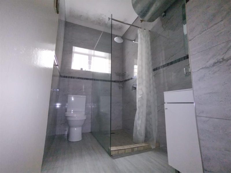 A compact bathroom featuring a glass-enclosed shower, toilet, and vanity cabinet, finished with grey wall and floor tiles.