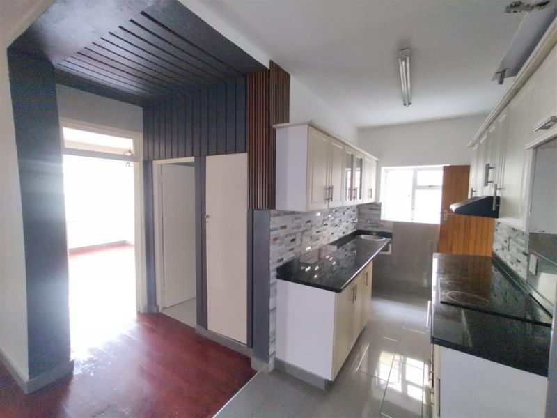 A clean, functional kitchen featuring granite countertops, built-in cabinetry, a tiled backsplash, and a distinctive timber ceiling detail, presented in an empty, well-maintained state.