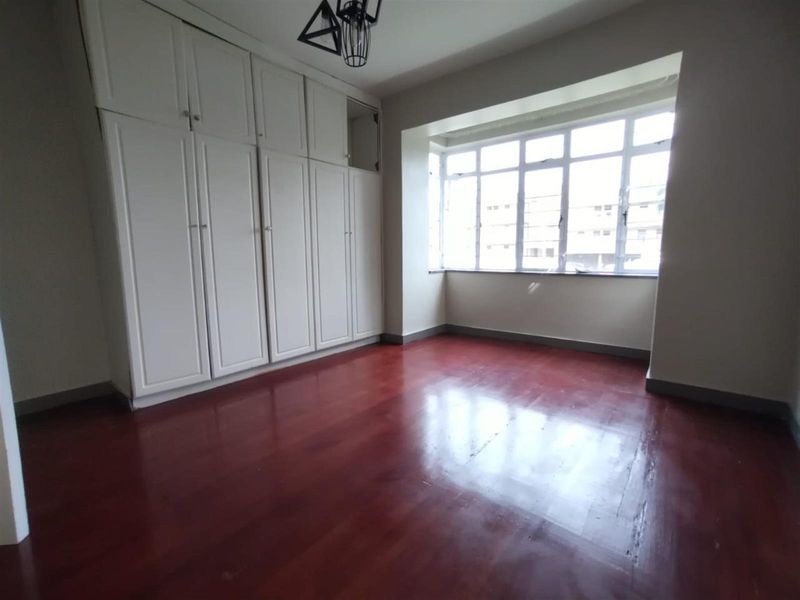 A bright, empty bedroom featuring polished hardwood flooring and extensive built-in storage cupboards, offering a clean and versatile living space.
