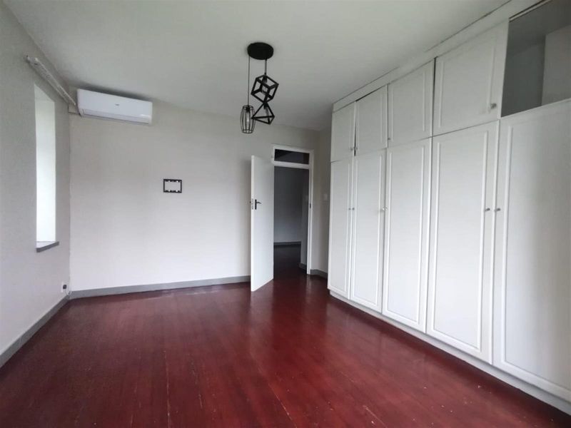 A bright, empty bedroom featuring polished hardwood flooring, extensive built-in storage cupboards, and a wall-mounted air conditioning unit.
