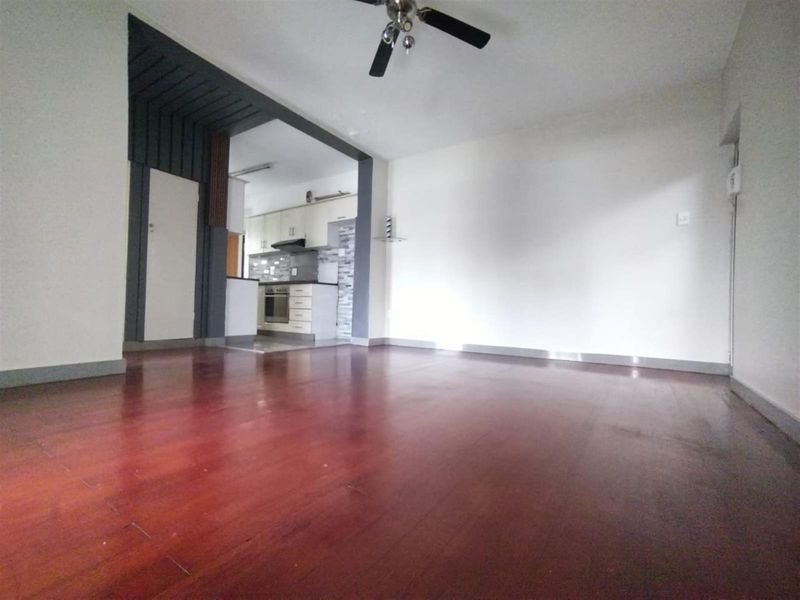 An open-plan living area featuring dark laminate flooring and a ceiling fan, leading into a functional kitchen with built-in cabinetry and appliances.