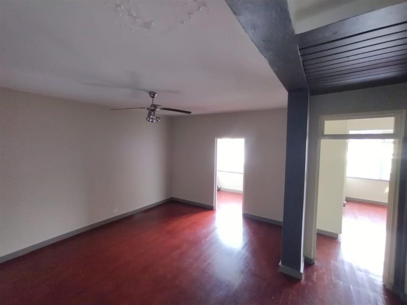 Spacious, empty living area featuring polished hardwood flooring, a ceiling fan, and decorative ceiling detailing, offering a blank canvas for personalization.