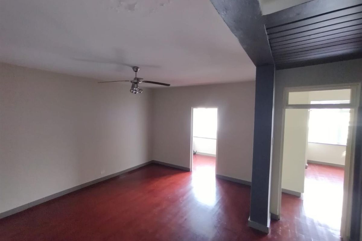 Spacious, empty living area featuring polished hardwood flooring, a ceiling fan, and decorative ceiling detailing, offering a blank canvas for personalization.