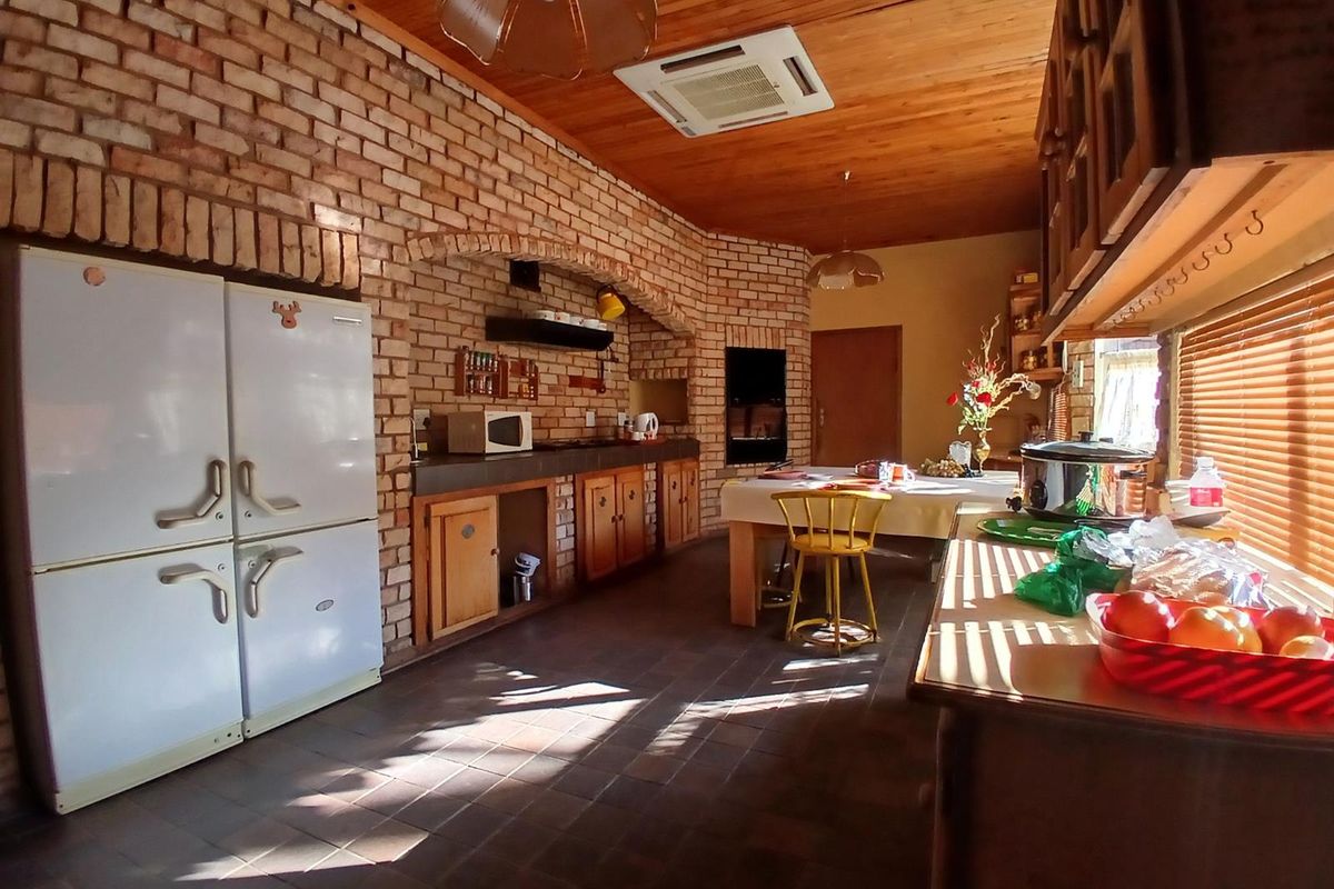 Spacious kitchen featuring exposed brick walls, timber ceiling, built-in cabinetry, and a large brick-surround cooking area.