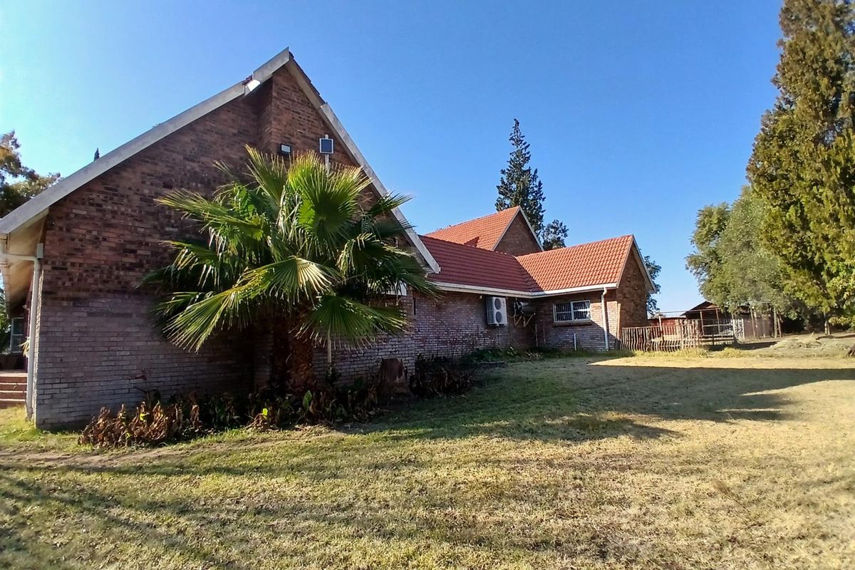 A view of the rear brick facade of the house, featuring a tiled roof, air conditioning unit, and surrounding garden space.