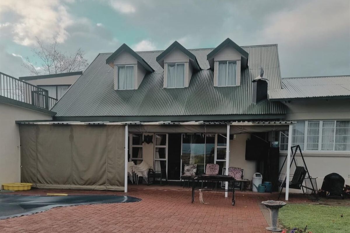 Rear view of the house featuring a covered patio area, brick paving, and a swimming pool, with dormer windows on the upper level.