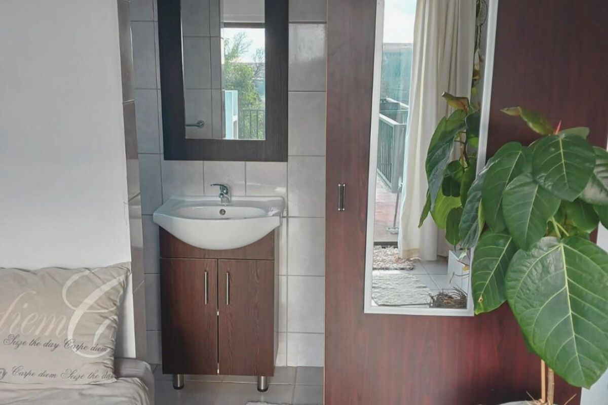 A compact bathroom area featuring a wall-mounted vanity with a basin, tiled splashback, and a mirror, adjacent to a wooden door with an integrated mirror.