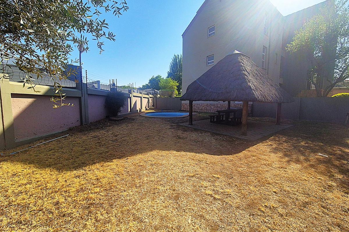 Rear garden area featuring a thatched lapa, a small swimming pool, and perimeter walling with security fencing.
