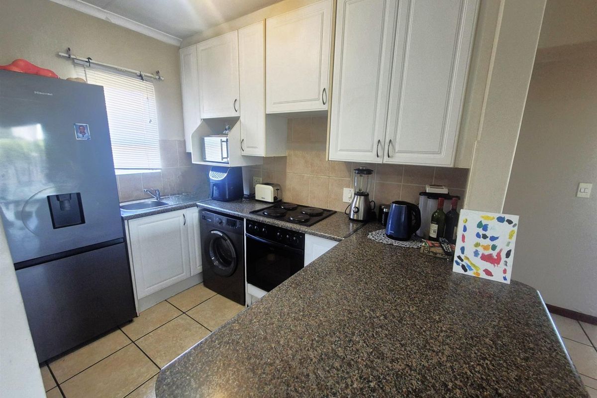 A functional kitchen featuring white cabinetry, granite-look countertops, tiled flooring, and integrated space for a washing machine and built-in oven.