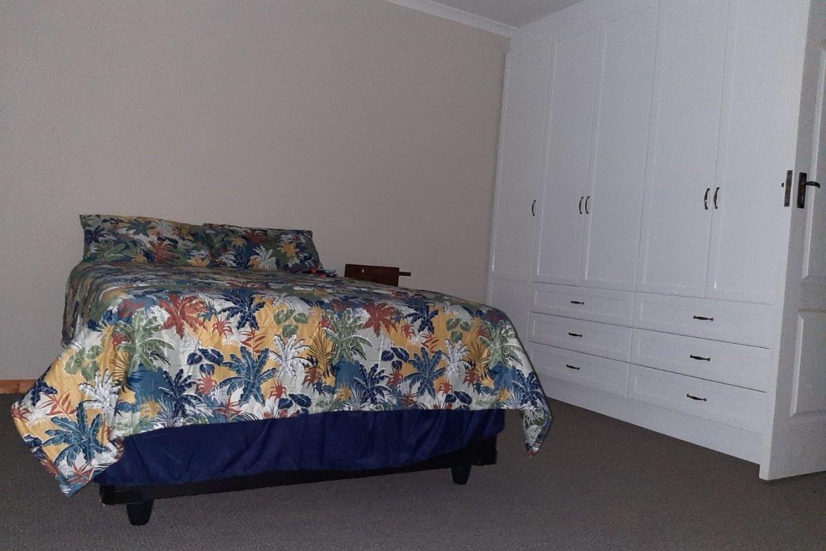 A bedroom featuring neutral wall tones, fitted white built-in cupboards with ample storage, and carpeted flooring.