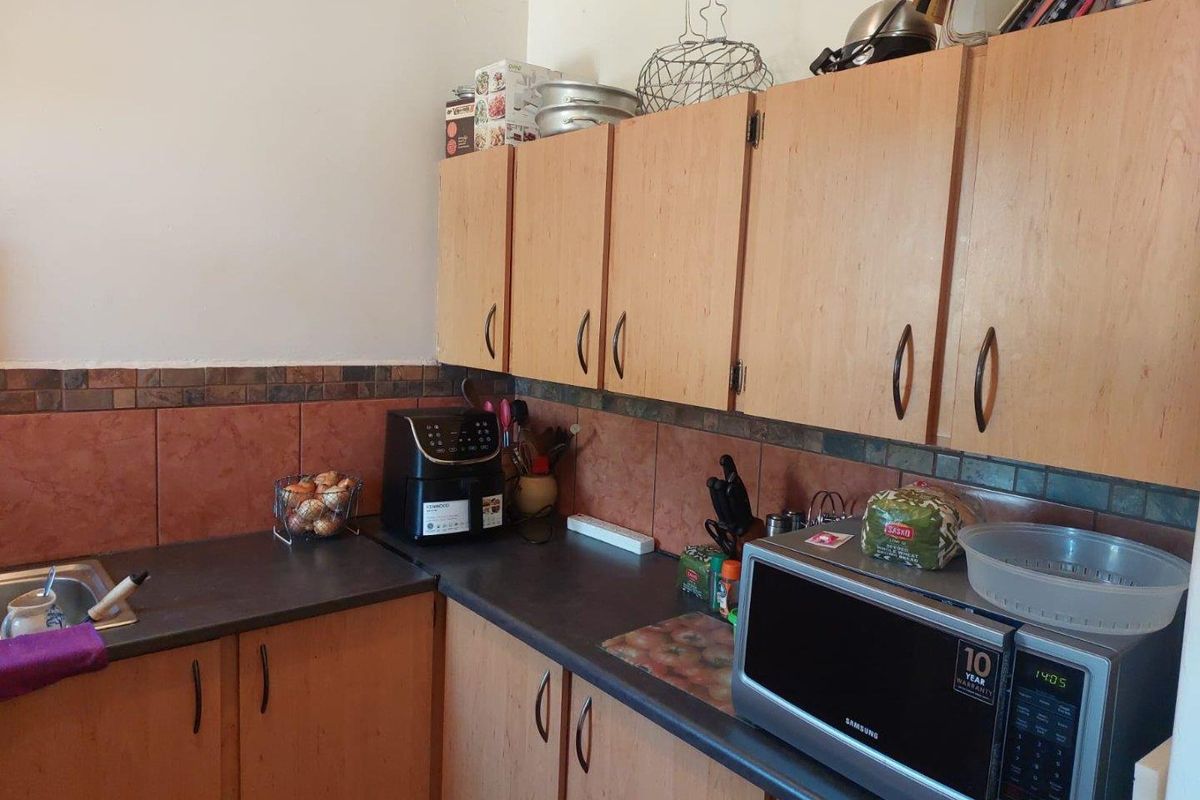 A functional kitchen area featuring light wood-finish cabinetry, dark laminate countertops, and decorative tiled splashbacks.