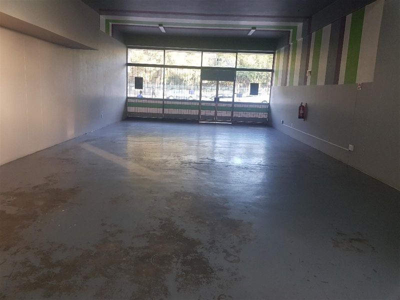 Spacious open-plan commercial unit featuring a large glass storefront, security gate, and durable concrete flooring, suitable for various retail or office applications.