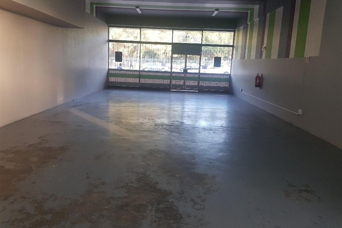Spacious open-plan commercial unit featuring a large glass storefront, security gate, and durable concrete flooring, suitable for various retail or office applications.
