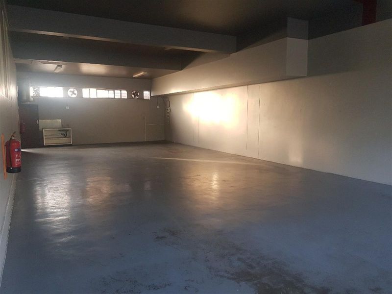 Spacious commercial utility area featuring durable epoxy flooring, integrated ventilation fans, and wall-mounted fire safety equipment, suitable for storage or workshop use.