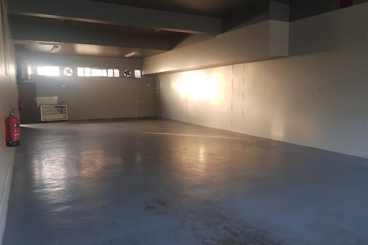 Spacious commercial utility area featuring durable epoxy flooring, integrated ventilation fans, and wall-mounted fire safety equipment, suitable for storage or workshop use.
