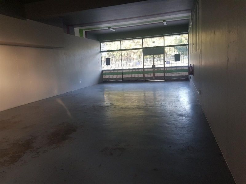 An empty, open-plan commercial space featuring a large glass storefront, security gate, and painted concrete flooring, suitable for various retail or office applications.