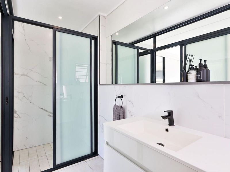 Modern bathroom featuring a walk-in shower with black-framed glass, a sleek vanity with a black mixer tap, and elegant marble-look wall tiles.