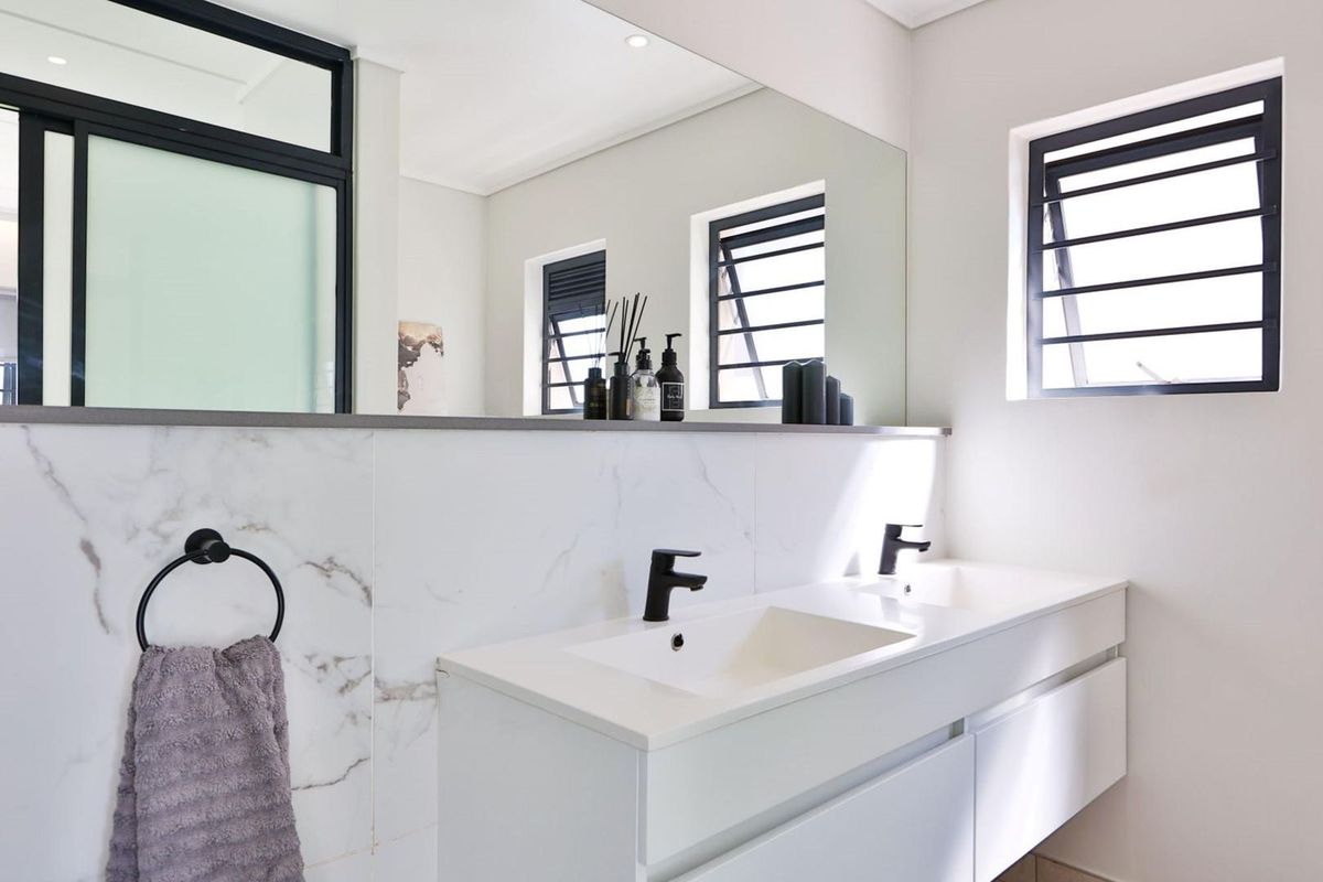 Modern bathroom featuring a sleek double vanity with black fixtures, marble-look wall tiling, and large mirror, complemented by louvered windows for natural light.