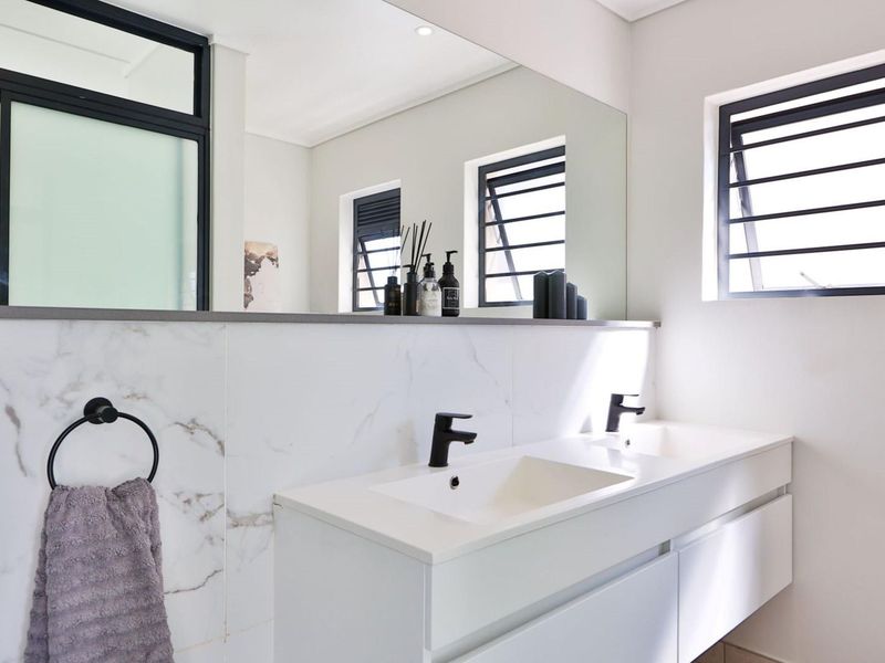 Modern bathroom featuring a sleek double vanity with black fixtures, marble-look wall tiling, and large mirror, complemented by louvered windows for natural light.