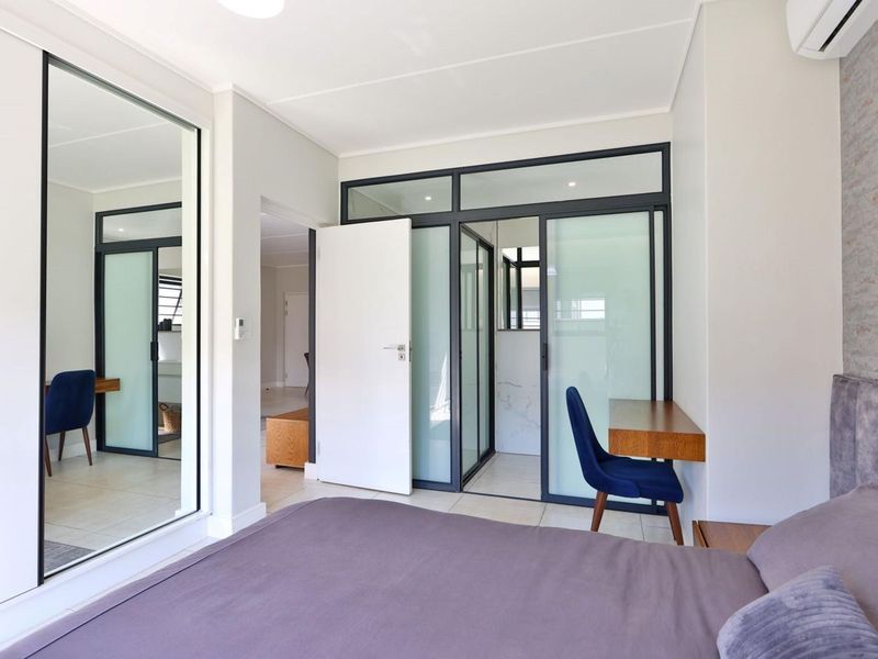 Modern bedroom featuring tiled flooring, built-in cupboards with mirrored doors, and a contemporary glass partition wall leading to an en-suite area.