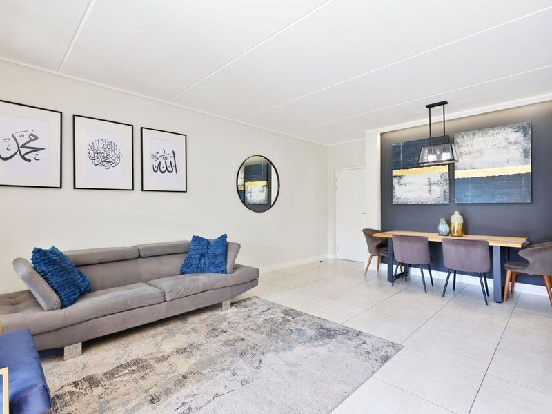 A bright and spacious open-plan living and dining area featuring neutral tiled flooring, a modern accent wall, and contemporary pendant lighting.
