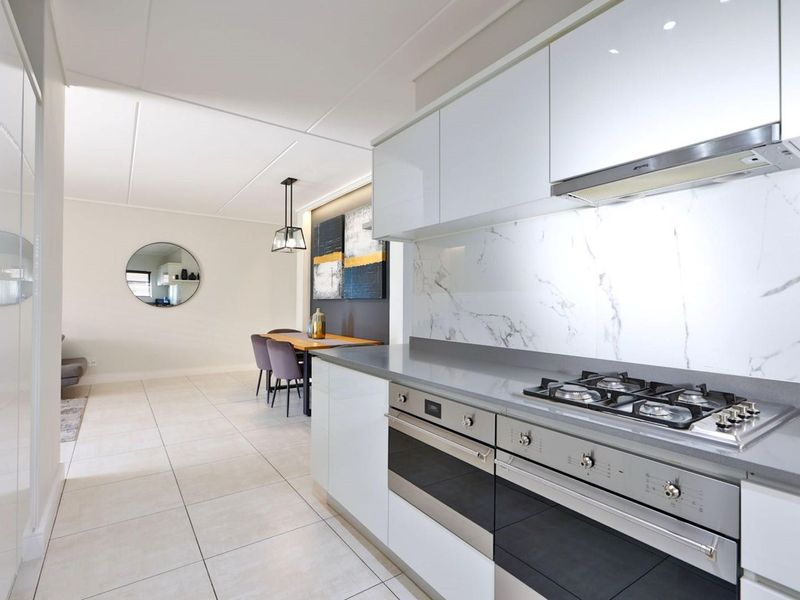 Modern open-plan kitchen and dining area featuring high-gloss cabinetry, integrated gas hob, built-in oven, and elegant marble-look splashback with neutral tiled flooring.