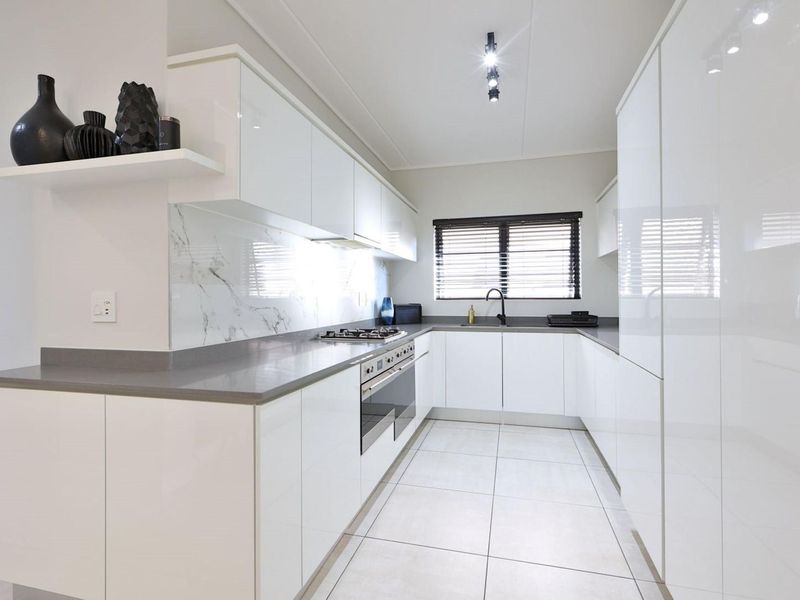 Modern kitchen featuring sleek white cabinetry, stone countertops, marble-look splashback, integrated appliances, and high-quality finishes throughout.