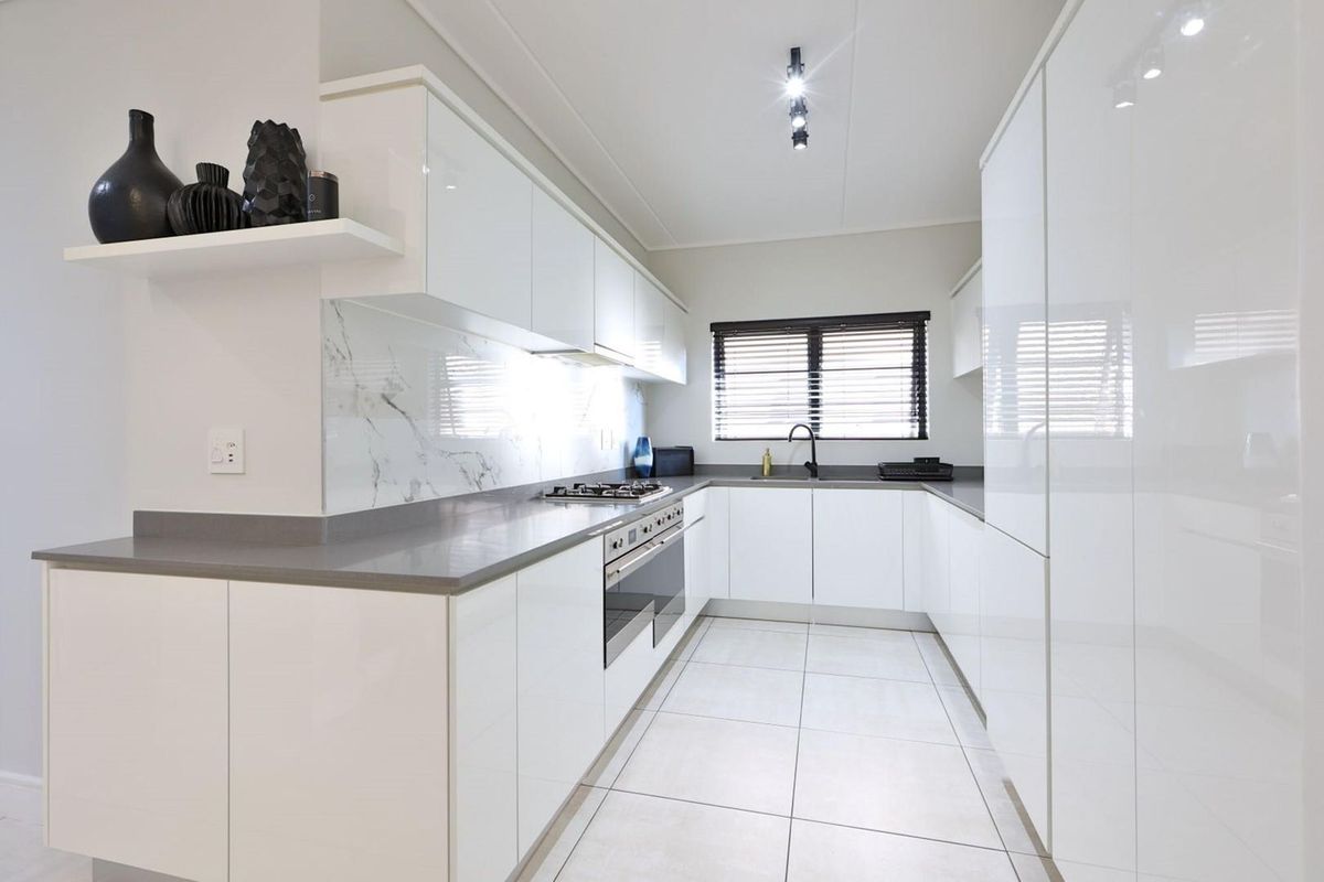 Modern kitchen featuring sleek white cabinetry, stone countertops, marble-look splashback, integrated appliances, and high-quality finishes throughout.