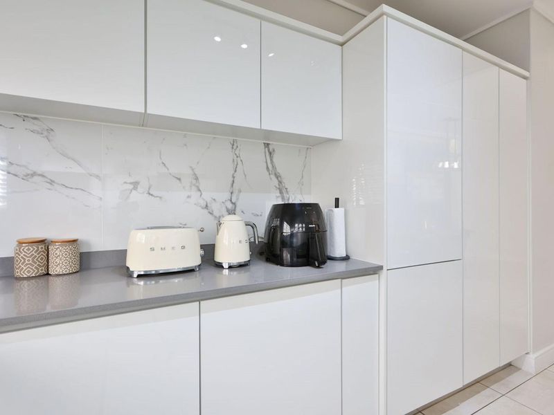 Modern kitchen featuring sleek glossy white cabinetry, stone countertops, and a sophisticated marble-look splashback, offering a clean and contemporary aesthetic.