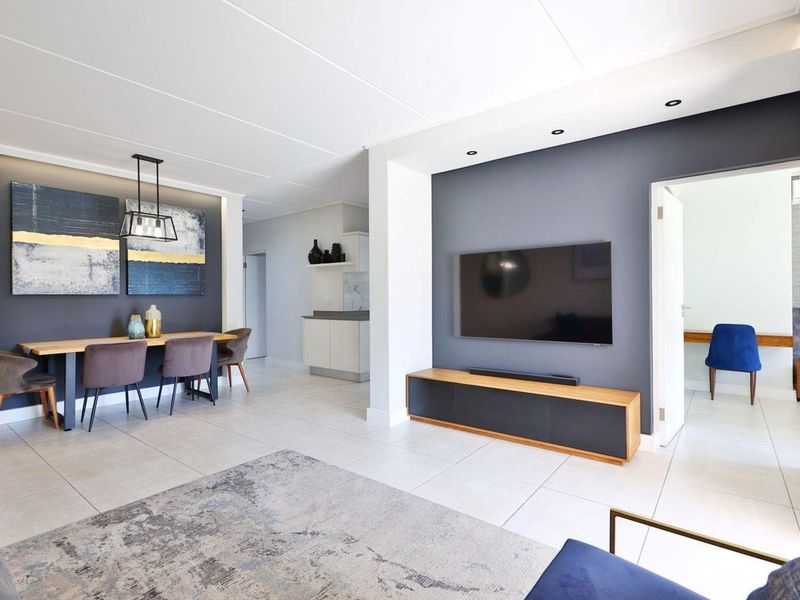 Modern open-plan living and dining area featuring neutral tiled flooring, recessed lighting, and a stylish dark grey accent wall.