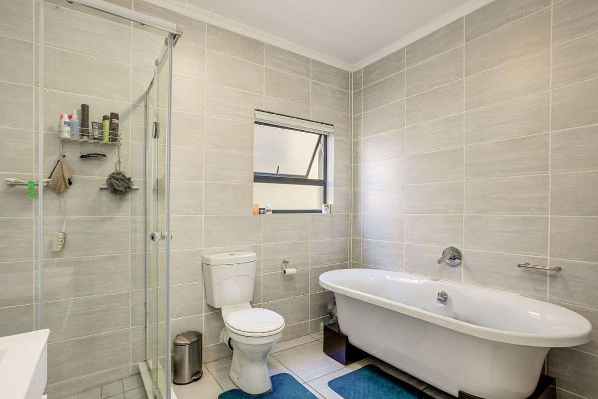 Modern bathroom featuring a freestanding bathtub, separate glass-enclosed shower, and neutral wall tiling.
