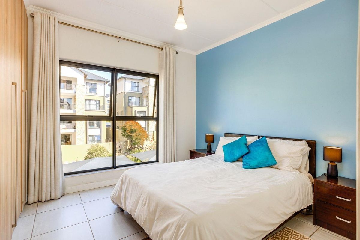 A bright bedroom featuring large windows, tiled flooring, and built-in wooden cabinetry, offering a comfortable living space with natural light.