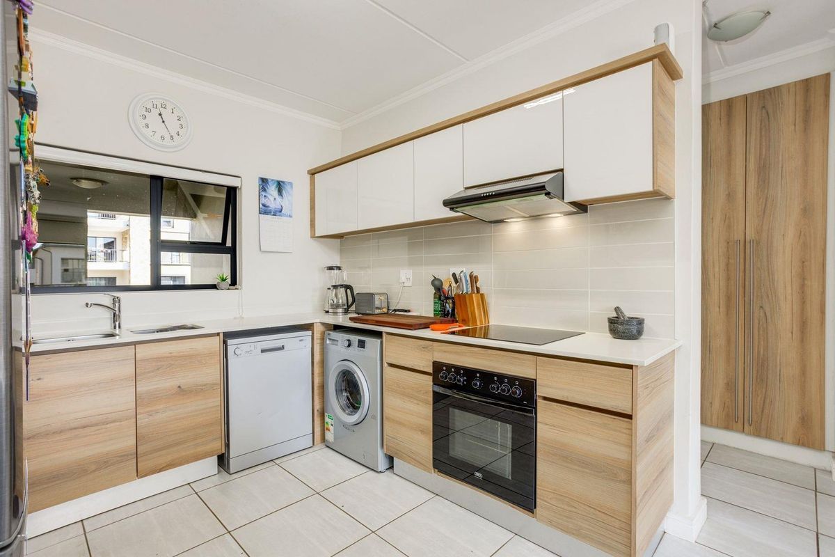 Modern kitchen featuring light wood-grain cabinetry, white countertops, integrated oven, hob, extractor fan, and tiled flooring.