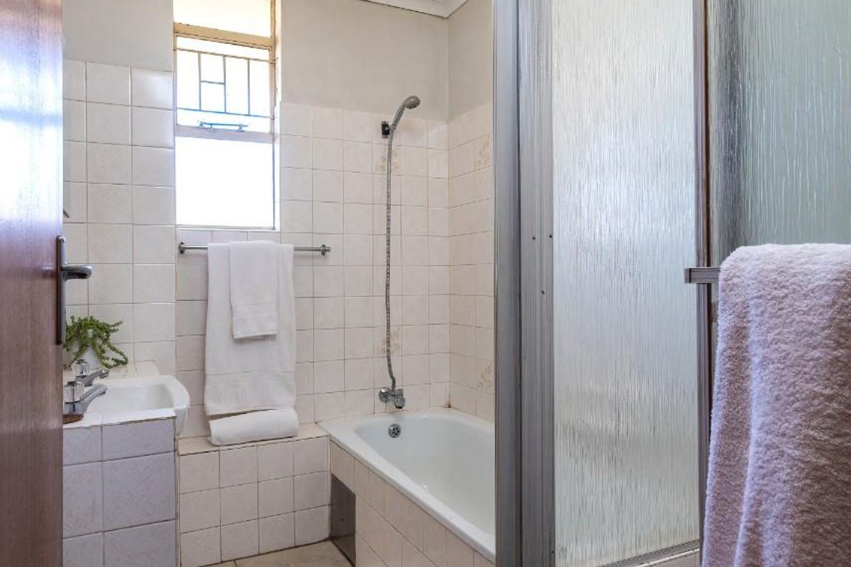 A functional bathroom featuring a built-in bathtub with shower attachment, tiled walls, and a separate shower enclosure with glass door.