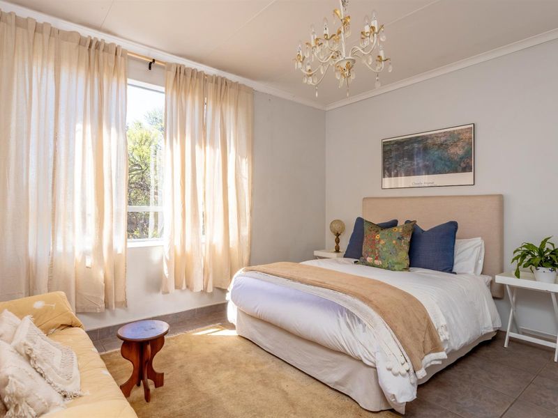 A well-lit bedroom featuring tiled flooring, a large window with natural light, and a decorative ceiling chandelier.
