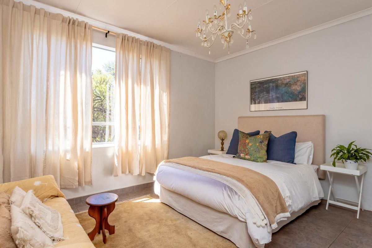 A well-lit bedroom featuring tiled flooring, a large window with natural light, and a decorative ceiling chandelier.