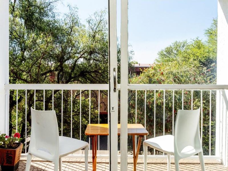 A compact balcony featuring tiled flooring and a white metal safety railing, offering a pleasant view of surrounding trees.