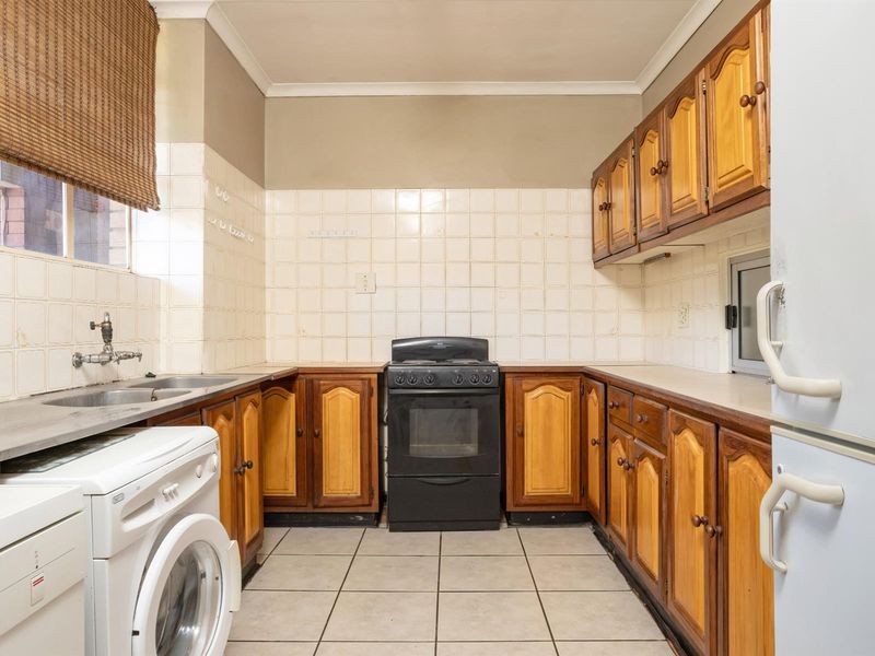 A functional kitchen featuring wooden cabinetry, tiled splashbacks, a built-in stove, and dedicated space for laundry appliances.