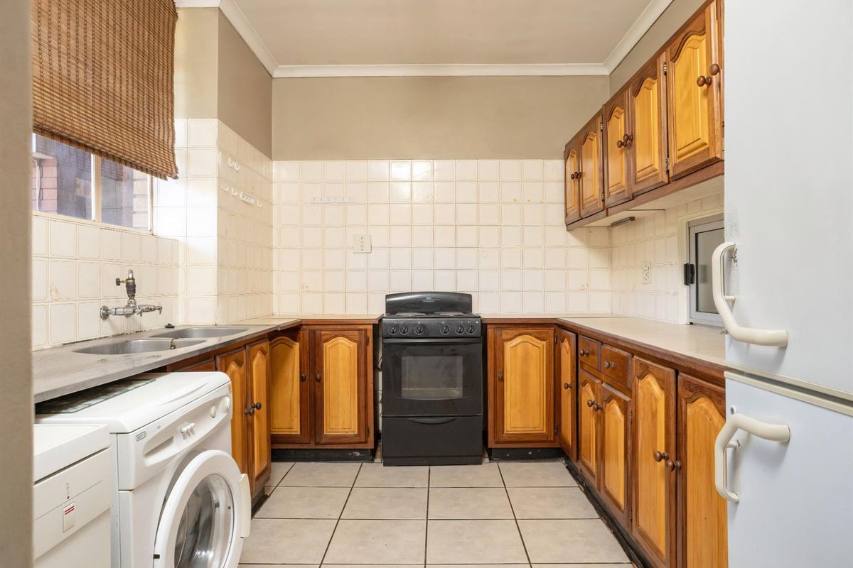 A functional kitchen featuring wooden cabinetry, tiled splashbacks, a built-in stove, and dedicated space for laundry appliances.