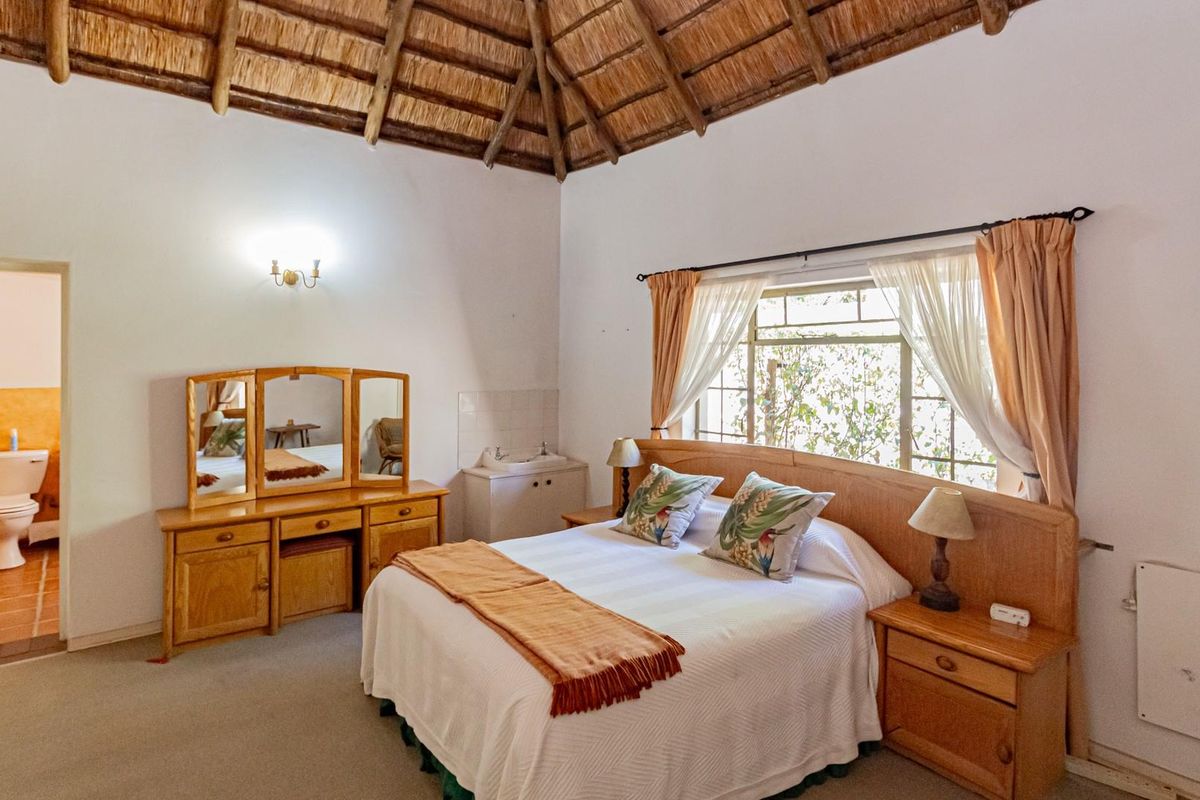A bedroom in a lodge featuring a traditional thatched roof, exposed timber rafters, and an en-suite bathroom with a toilet.