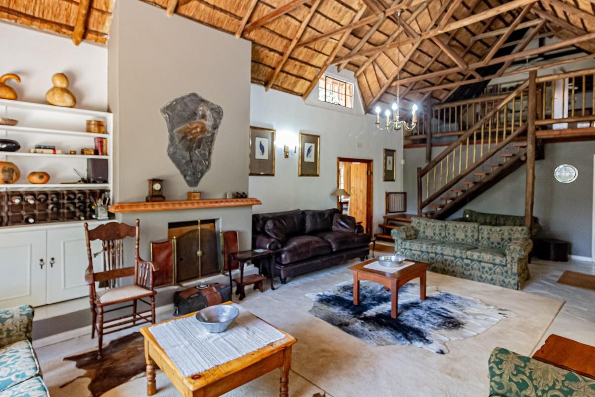 Spacious living room featuring a high vaulted thatch ceiling with exposed timber trusses, a central fireplace, and a wooden staircase leading to a mezzanine level.