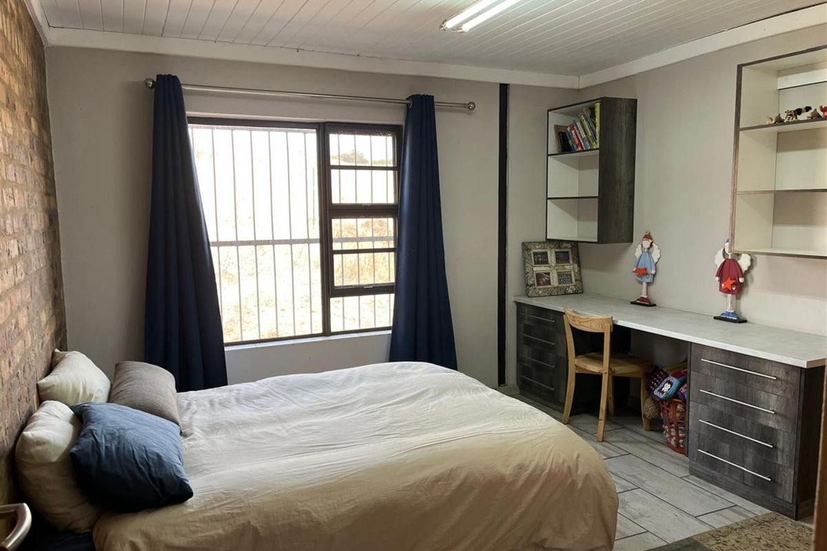 A functional bedroom featuring built-in desk cabinetry, shelving, tiled flooring, and a window with security bars.