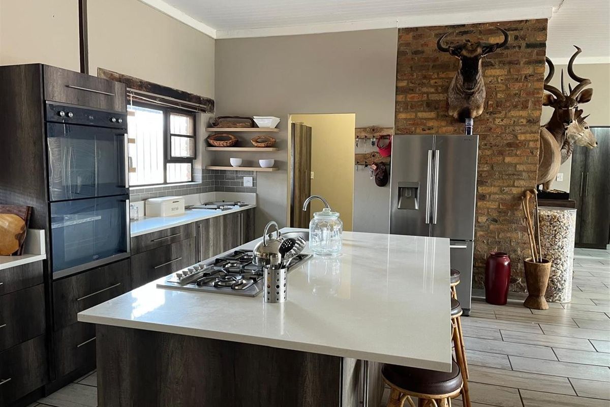 Modern kitchen featuring a central island with a built-in gas hob, dark wood cabinetry, stone countertops, and an exposed brick feature wall.