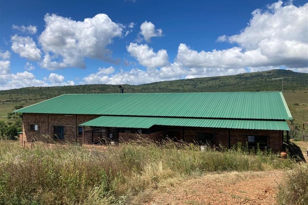 A view of the farm property featuring a brick exterior with a green corrugated metal roof set against a rural landscape.