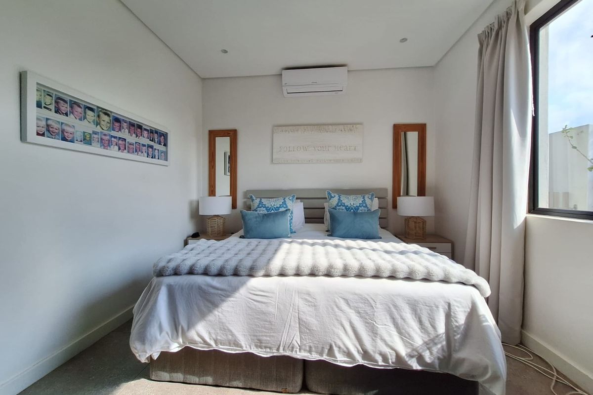 A well-maintained bedroom featuring tiled flooring, recessed downlighting, and a wall-mounted split-system air conditioning unit.