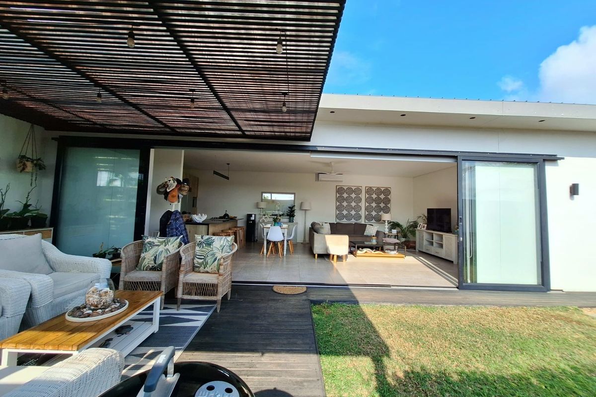 Spacious covered patio featuring timber decking and a pergola, seamlessly connecting to the open-plan interior living area through large sliding glass doors.