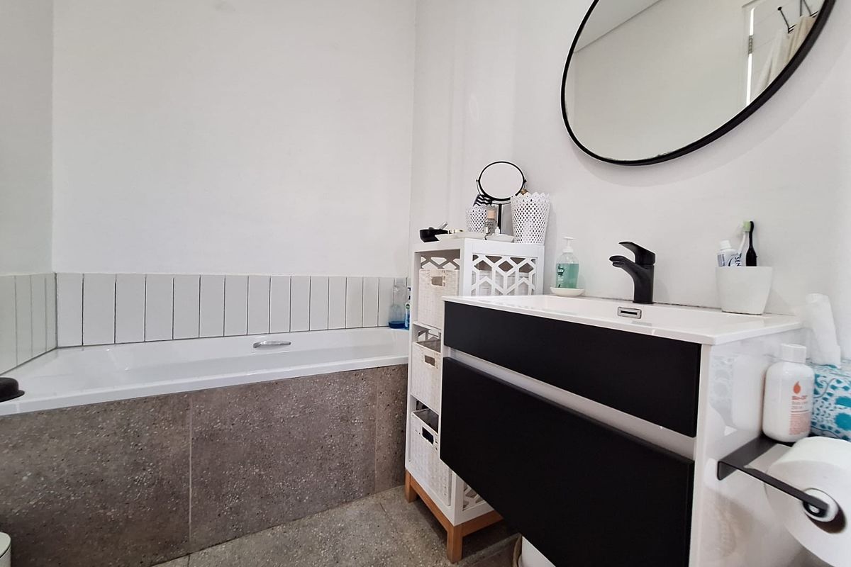 Modern bathroom featuring a built-in bathtub with tiled surround, a contemporary vanity cabinet with a black mixer tap, and a wall-mounted mirror.